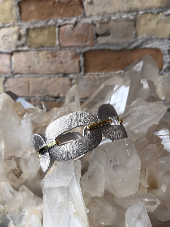 Photo of Textured Buckle Bangle in a decorative scene, designed by , available at Plumb Gold & Plumb Silver