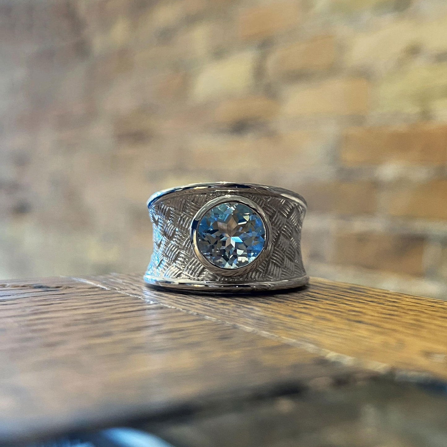 Photo of Wide Basket-Weave Ring with Blue Topaz Center in a decorative scene, designed by , available at Plumb Gold & Plumb Silver
