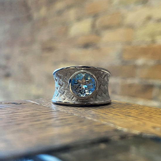 Photo of Wide Basket-Weave Ring with Blue Topaz Center in a decorative scene, designed by , available at Plumb Gold & Plumb Silver