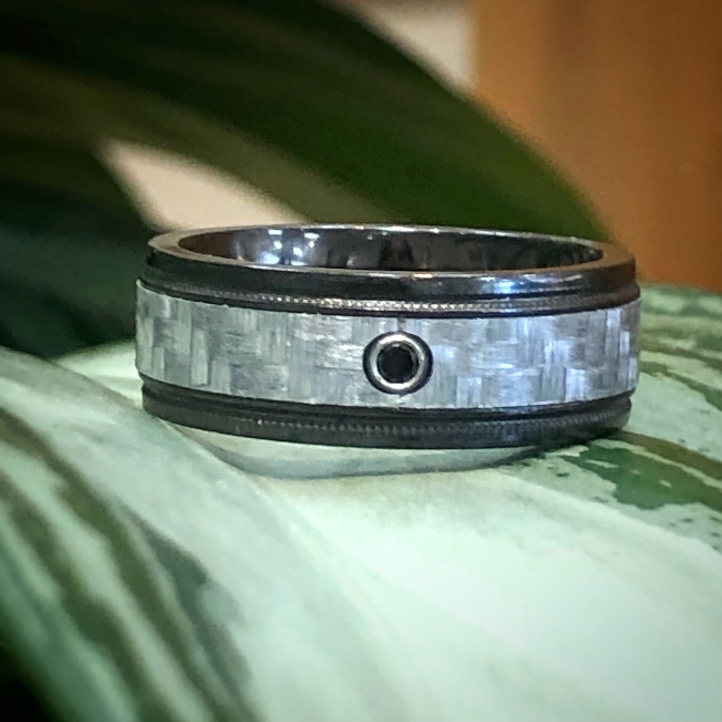 Photo of Zirconium and Silver Carbon Fiber Black Diamond Band in a decorative scene, designed by , available at Plumb Gold & Plumb Silver