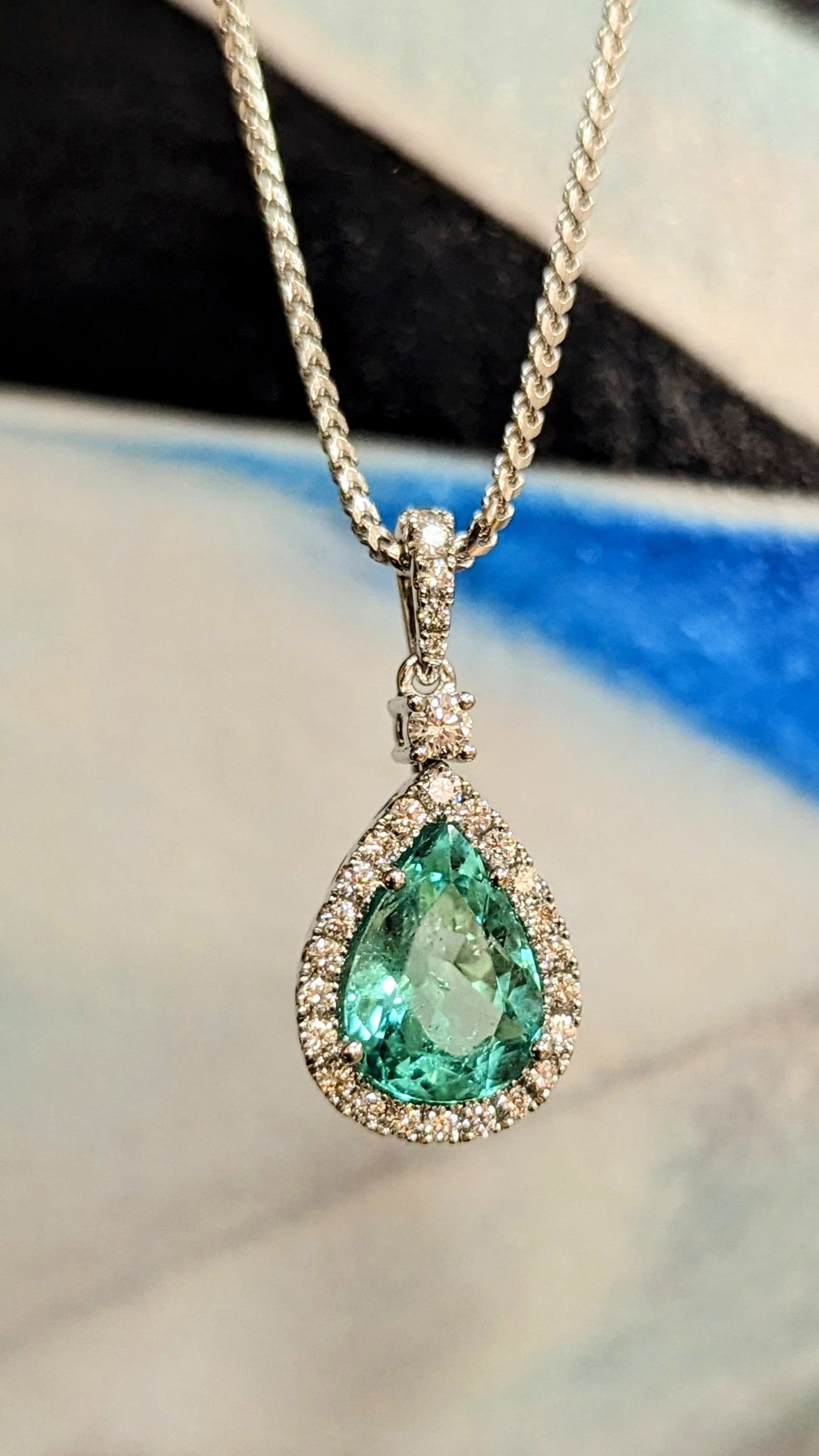 Photo of Zoma Color Emerald Halo Pendant in a decorative scene, designed by , available at Plumb Gold & Plumb Silver
