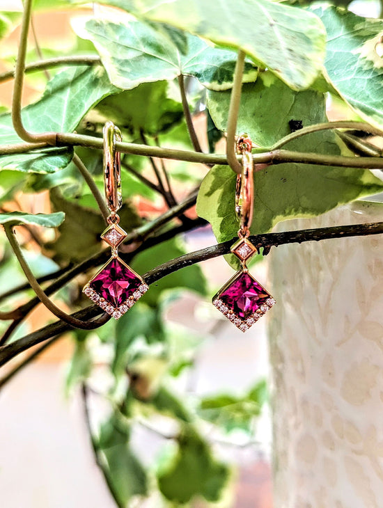 Photo of Zoma Color Rubellite and Diamond Dangle Earrings in a decorative scene, designed by , available at Plumb Gold & Plumb Silver