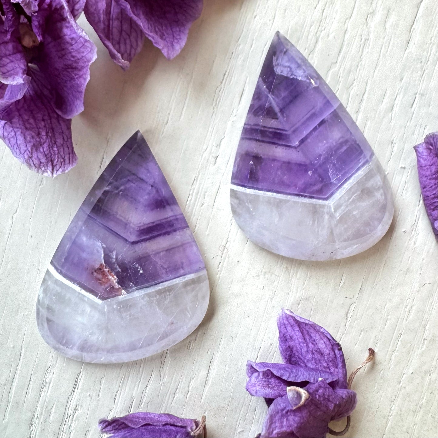 Teardrop-shaped purple and white stones on a light wooden surface with purple flowers.
