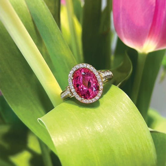 Pink tourmaline and diamond halo ring sitting on  a tulip leaf